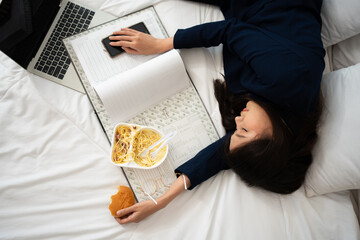 Busy and tired businesswoman eating bread for breakfast in bed at home and working to deliver...