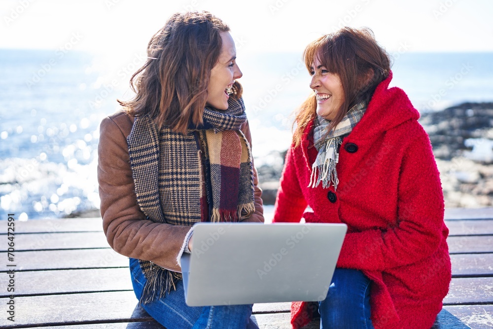 Poster Two women mother and daughter using laptop sitting on bench at seaside