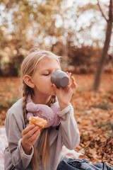 A girl on a picnic in an autumn park eats a croissant.