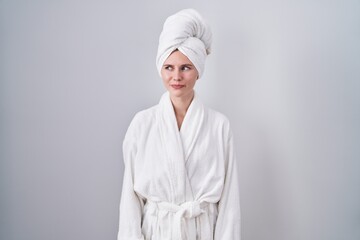 Blonde caucasian woman wearing bathrobe smiling looking to the side and staring away thinking.