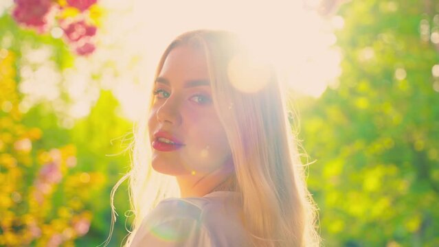 Young sexy happy woman looking back beauty face long blond hair fly in wind motion, elegant lady. Stylish luxury girl, natural make-up walks in green sping garden park rear view, magical sun light 4k