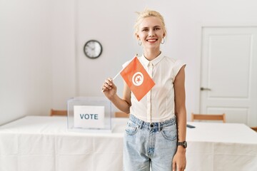 Young blonde woman holding tunisia flag smiling at electoral college