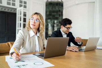 Focused businesswoman with glasses working alongside male colleague in a modern office.