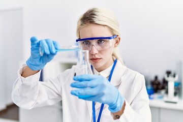 Young blonde woman scientist pouring liquid on test tube at laboratory