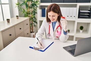 Young blonde woman doctor writing medical report holding empty test tube at clinic