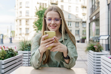 Urban professional happily using her smartphone at a street cafe, modern city life.