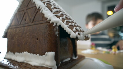 Decorating gingerbread house with royal ice ornament on top of traditional festive Christmas dessert