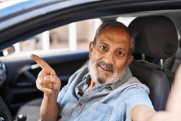 Cheerful senior man happily pointing to a car while making a joyful selfie outdoors in the city