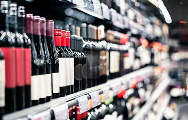 Liquor store, alcohol shop. Red wine on shelf. Focus on bottles, supermarket aisle in background. Alcoholic drink sale and selection in grocery market. Pinot noir, merlot or sauvignon cabernet. - obrazy, fototapety, plakaty