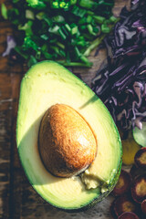 Avocado halves on the kitchen table with chopped fresh vegetables.