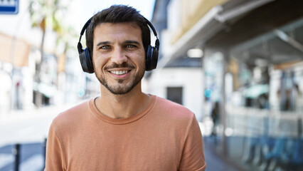 Smiling young hispanic man with headphones standing on a busy city street