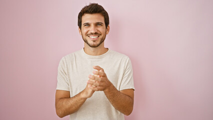 Smiling young hispanic man with a beard, clapping hands against a pink isolated background.
