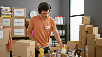 A young adult man volunteering, organizing donations indoors at a center, wearing headphones.