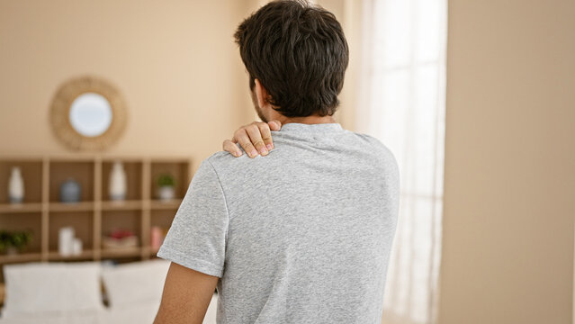 Rear view of a young man with a shoulder pain in a modern living room.