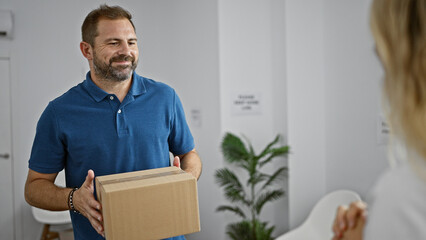 Hispanic mature man with grey hair handing over a package indoors, evoking a friendly delivery in a...