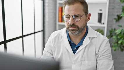 Hispanic mature man with grey hair in lab coat working indoors at clinic.