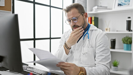 A pensive middle-aged man with grey hair, wearing a stethoscope, reviews documents in a hospital...