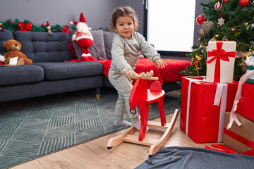 Adorable hispanic toddler playing with reindeer rocking by christmas tree at home