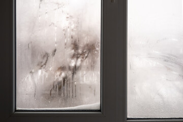 Nostalgic winter mood. Wet with condensation and frozen window with unclear winter view. View from interior of a room.