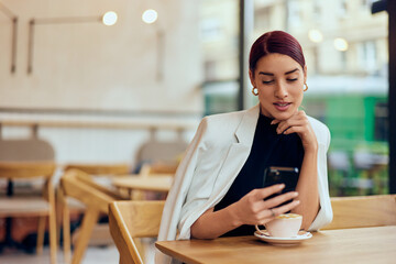 A beautiful woman sitting at the cafe bar alone, using a mobile phone, dressed fashionably.