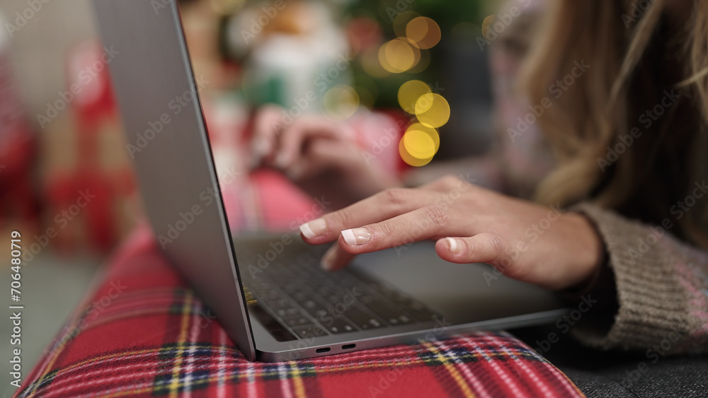 Sticker Young blonde woman using laptop lying on sofa by christmas tree at home