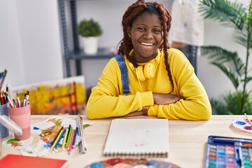 African american woman artist smiling confident sitting on table at art studio