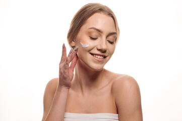 Beauty portrait of a beautiful blonde girl applying cream on her face on an isolated white background
