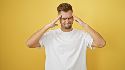 Fototapeta na wymiar A stressed hispanic man in a white shirt with a beard stands against a yellow background, showing a headache.
