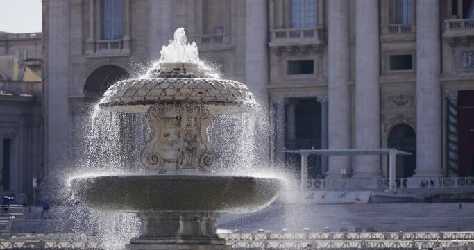 Cinematic view of the fountain on the Saint Peter square outside the vatican with water flow spray in slow motion, establishing shot