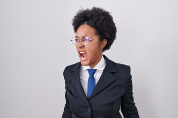 Beautiful african woman with curly hair wearing business jacket and glasses angry and mad screaming...