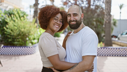 Fototapeta premium Beautiful couple, full of joy and positivity, hugging and sharing a sunny laugh in an outdoor park. casual, fun love, their confident smiles radiating happiness.