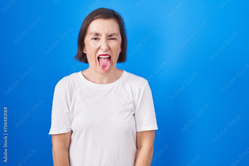 Canvas Prints Middle age hispanic woman standing over blue background sticking tongue out happy with funny expression. emotion concept.