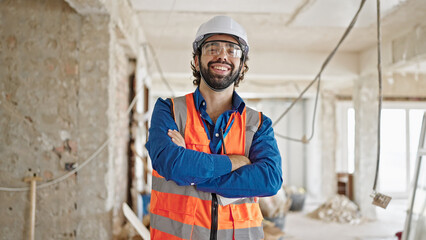 Young hispanic man architect smiling confident standing with arms crossed gesture at construction site - Powered by Adobe