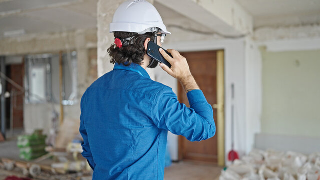 Young hispanic man architect standing backwards talking on smartphone at construction site