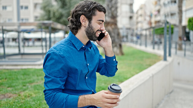 Young hispanic man talking on smartphone drinking coffee at park