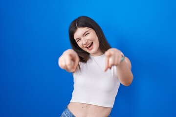 Fototapeta na wymiar Young caucasian woman standing over blue background pointing to you and the camera with fingers, smiling positive and cheerful