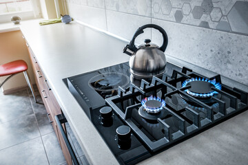 Steel kettle with whistle on modern burning gas stove