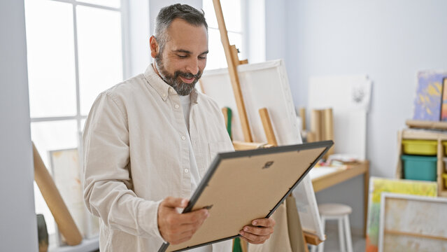 Handsome bearded senior man examining artwork in a bright studio interior, embodying creativity and experience.
