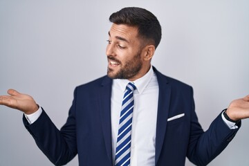 Handsome hispanic man wearing suit and tie smiling showing both hands open palms, presenting and advertising comparison and balance