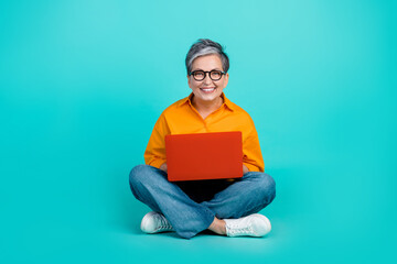 Full length photo of white haired woman sitting floor with netbook learning new python programming code isolated on cyan color background