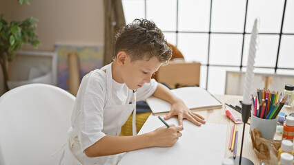 Adorable little blond boy artist intently drawing in his notebook, immersed in art class at the...
