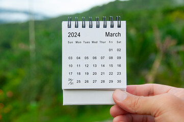 Hand holding March 2024 white calendar with nature background. Holiday and calendar concept