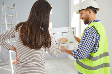 Foreman showing blueprint to young homeowner woman of design project or repair of her new apartment...