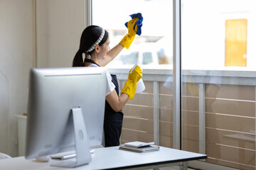 Young female cleaner is spraying cleaning solution on the glass and is wiping the window glass at...