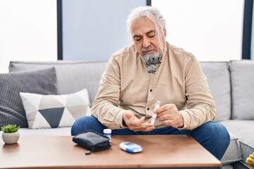 Middle age grey-haired man measuring glucose sitting on sofa at home