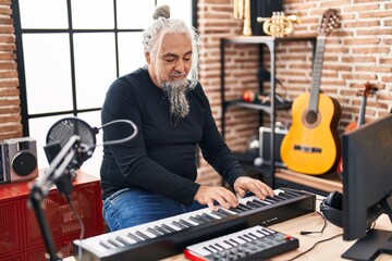 Middle age grey-haired man musician playing piano at music studio