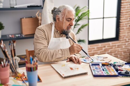 Middle age grey-haired man artist drawing on notebook with relaxed expression at art studio