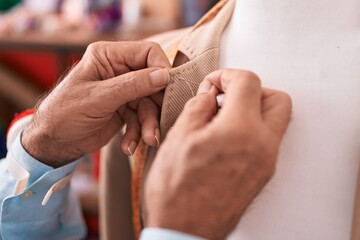 Middle age grey-haired man tailor sewing jacket on manikin at atelier