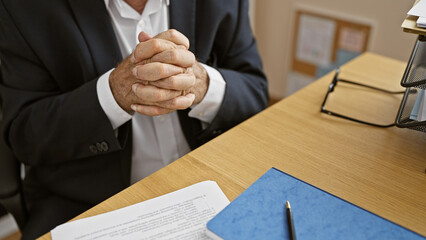 Senior man hands visibly hard-at-work, clasped together on an office table, embodying the relaxed confidence of a successful business professional.