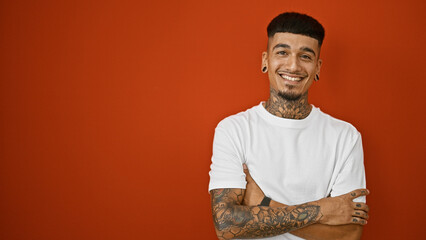 Confident latin young man, casually tattooed, poses with arms crossed, smiling at camera with joy,...